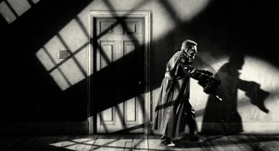 Sin City (2005) movie still: medium — A dimly lit interior space features a closed door set in a textured wall. A man wearing a long coat moves past…