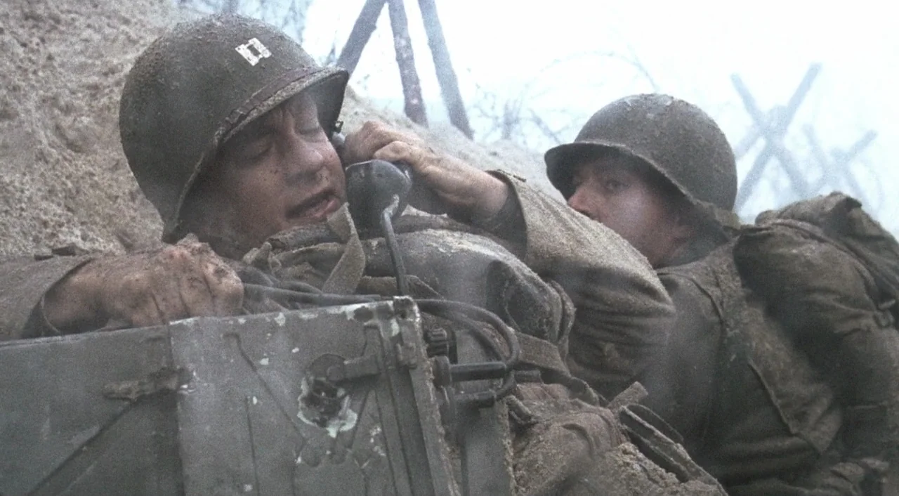 Saving Private Ryan (1998) movie still: medium — A muddy trench line features two soldiers in World War II gear. One soldier communicates over a…