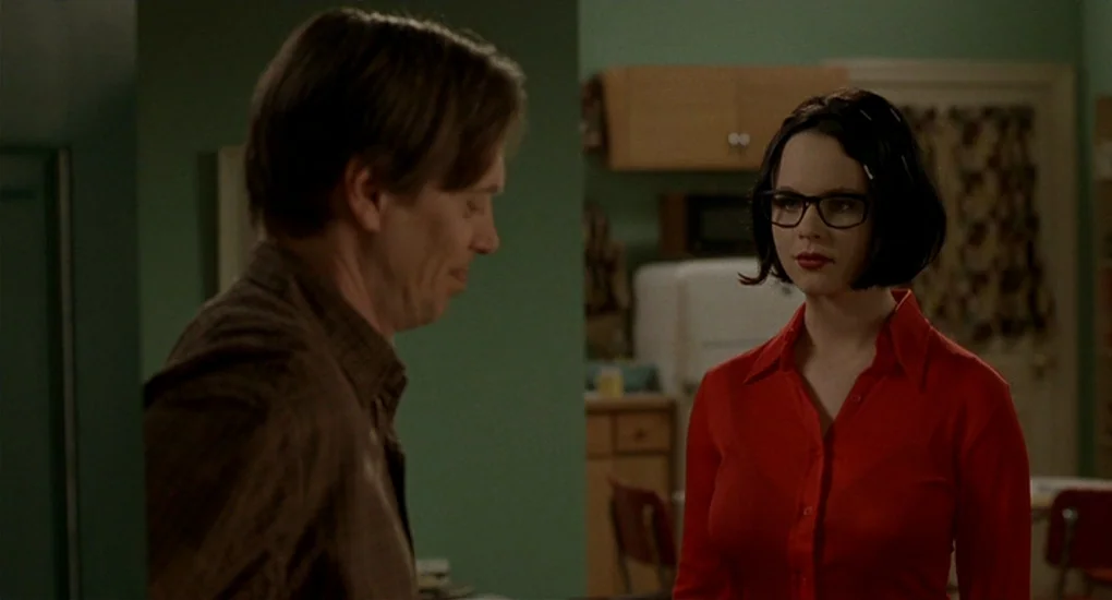 Ghost World (2001) movie still: medium — A residential room features olive green walls and light wood cabinets in the background. A woman in a red…