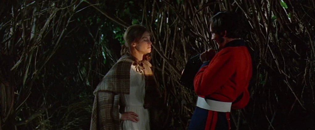 Far from the Madding Crowd (1967) movie still: medium — A man in a 19th-century red military uniform stands amidst dense, shadowed tree branches.…