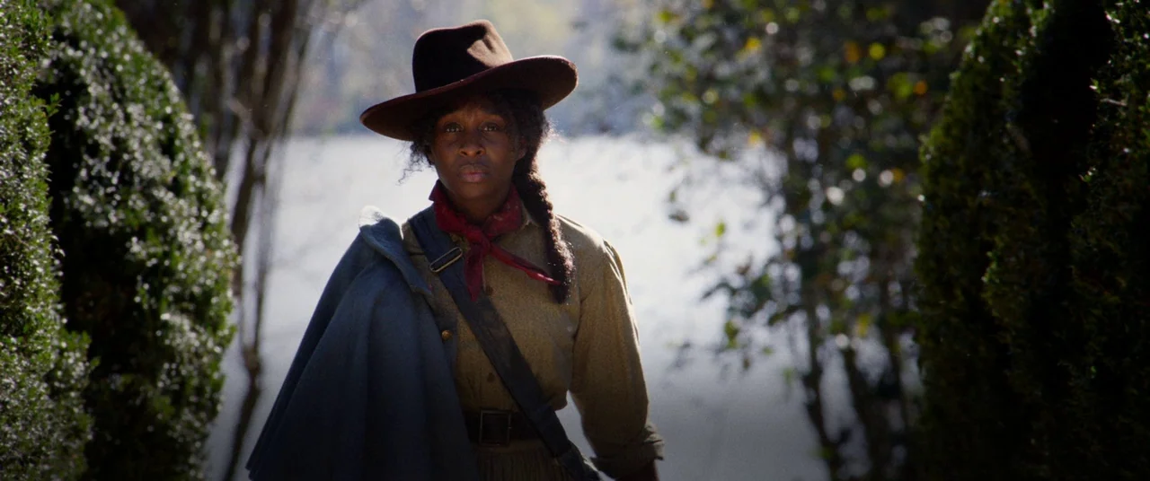 Harriet movie still: medium — A woman walks along a narrow trail surrounded by dense trimmed bushes and trees. She is dressed in nineteenth-century…