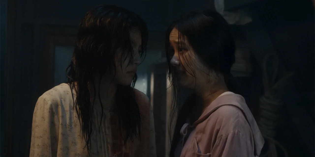 Host (2020) movie still: medium — A dark indoor setting with limited visibility and shadowy surroundings. Two women with damp hair stand close…