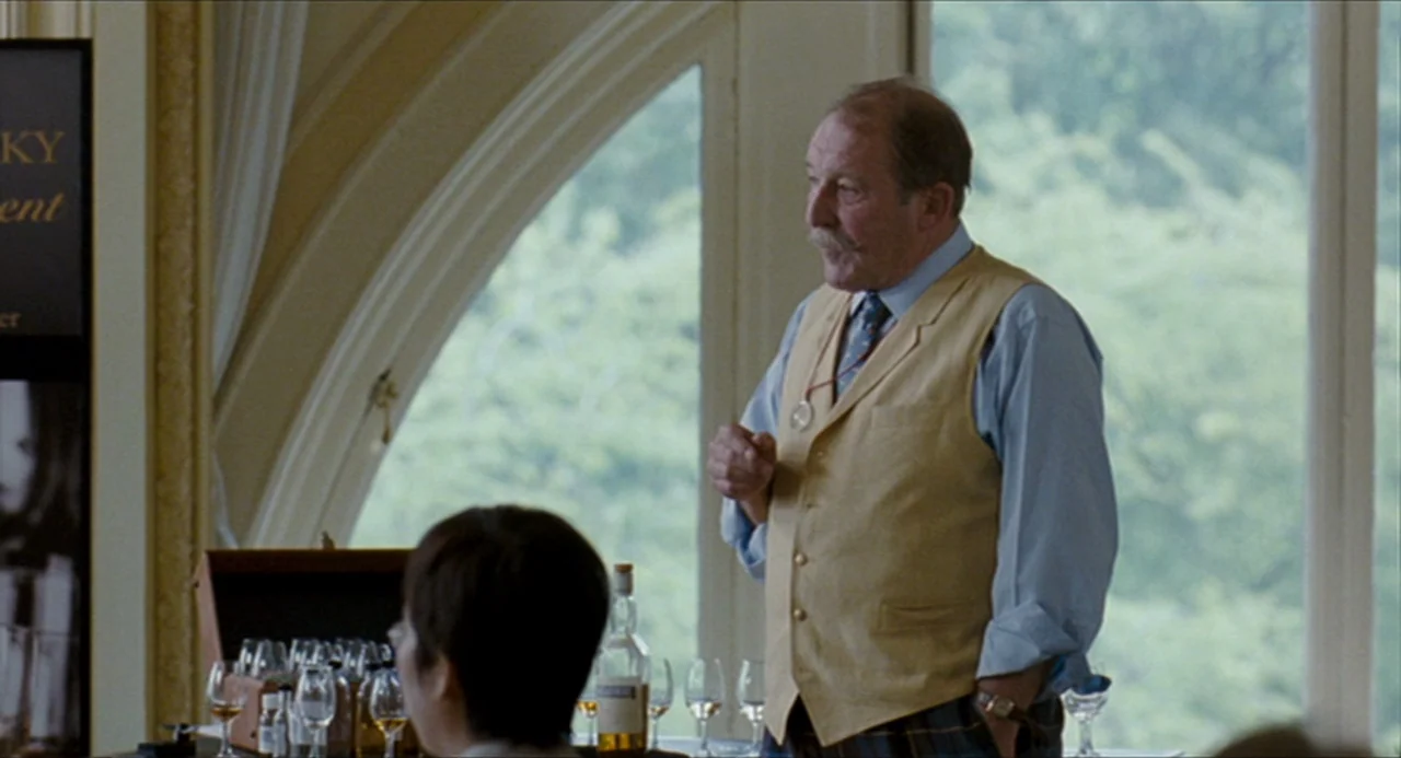 The Angel’s Share (2012) movie still: medium — An interior space features large arched windows looking out onto green trees. An older man stands…