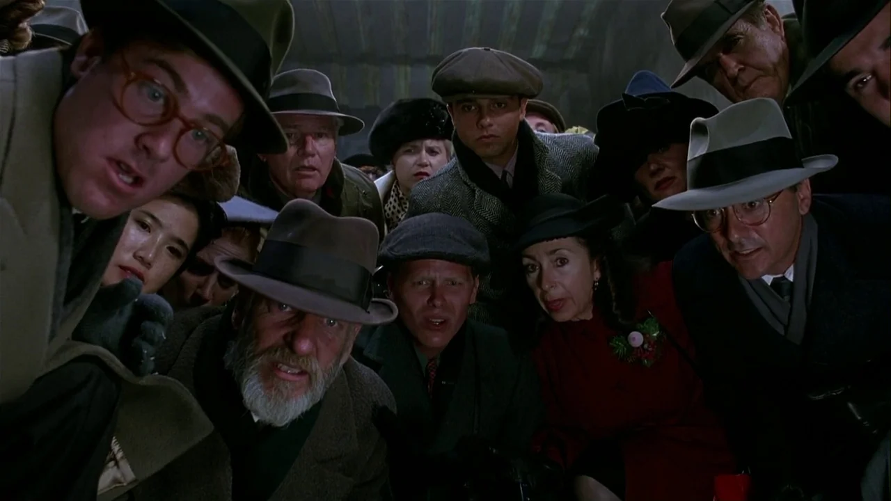 Batman Returns (1992) movie still: medium — A diverse crowd of people in period-appropriate attire huddles together tightly indoors. They stare…