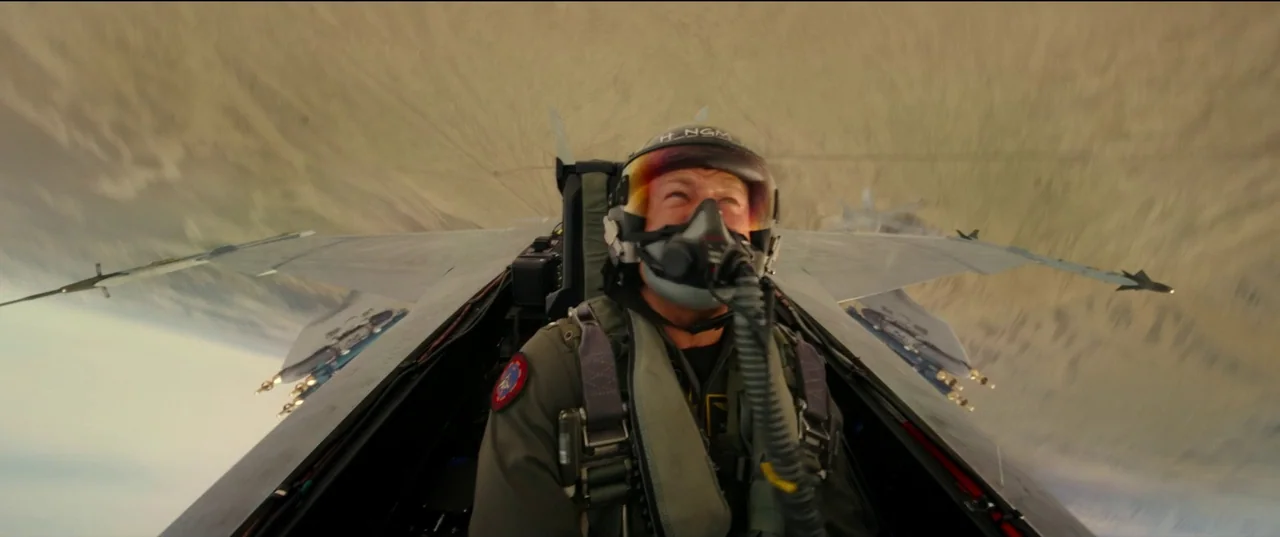 Top Gun: Maverick (2022) movie still: medium — A fighter jet cockpit flying at high speed above a blurred desert landscape. A pilot in a flight suit…