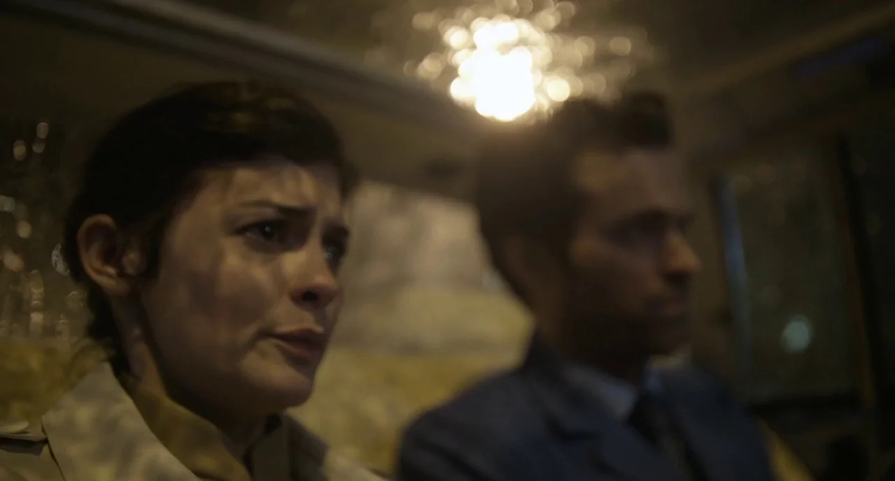 Mood Indigo (2013) movie still: medium — An interior of a vehicle at night with shallow depth of field. A woman in a tan coat sits beside a man…