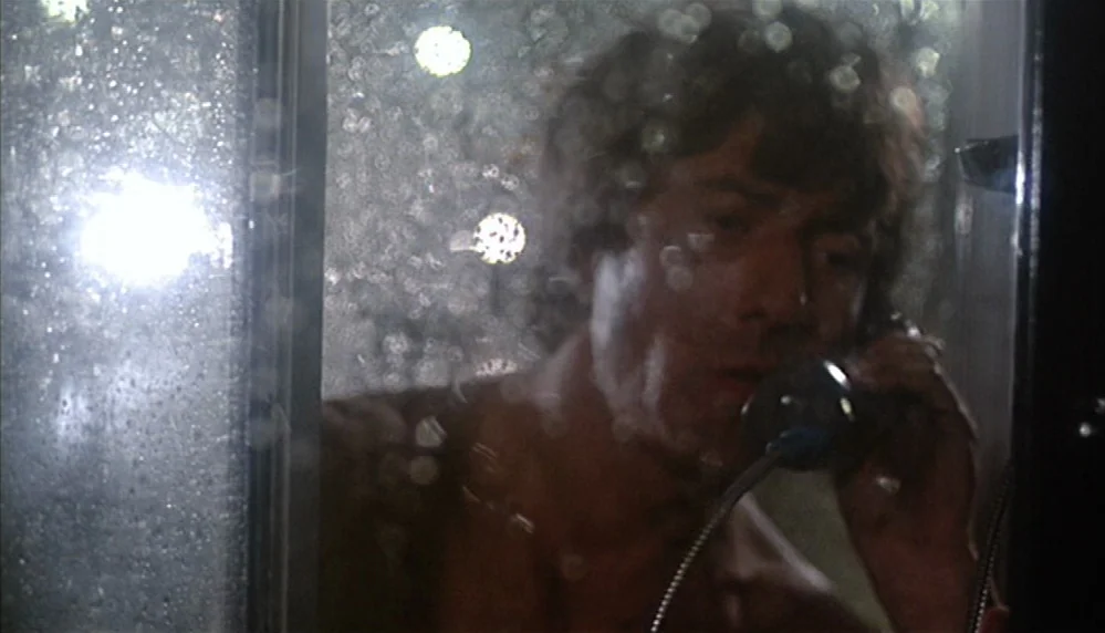Marathon Man (1976) movie still: closeup — A rain-streaked glass enclosure illuminated by distant out-of-focus street lights at night. A man with…