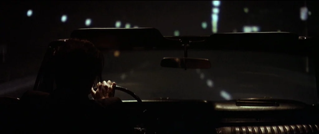 Pulp Fiction (1994) movie still: medium — The interior of a vehicle moving along a dark highway at night. A lone driver is visible in silhouette…
