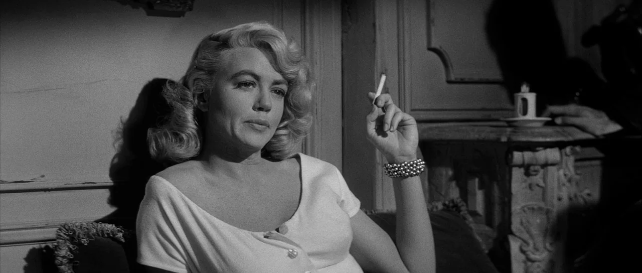 The Tarnished Angels (1957) movie still: medium — A classic interior setting features ornate wall moldings and a small table with a lamp. A woman…