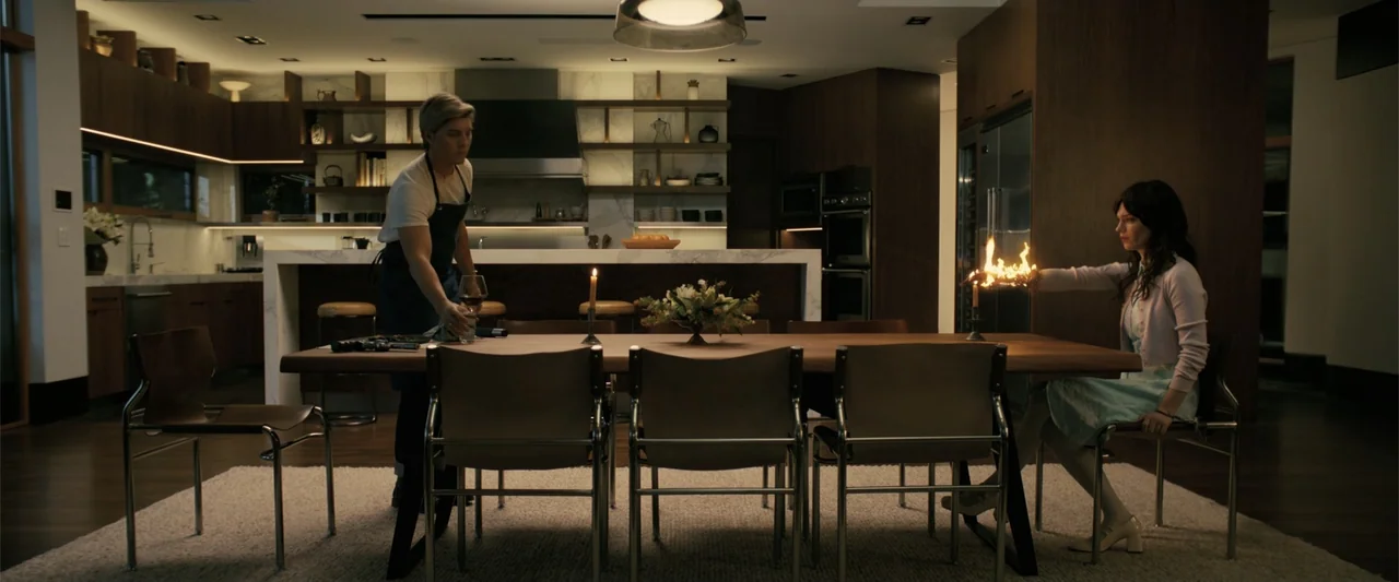 Companion (2025) movie still: wide — A spacious modern home features dark wood cabinetry and a marble-topped island background. A man stands by a…