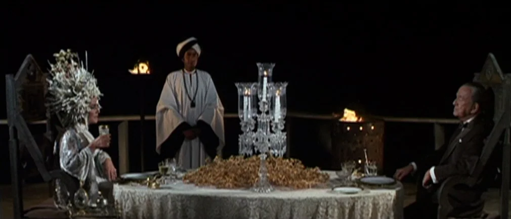 Boom! (1968) movie still: wide — A nighttime dinner setting on a terrace features a white-clothed table with a crystal candelabra. A man and a woman…