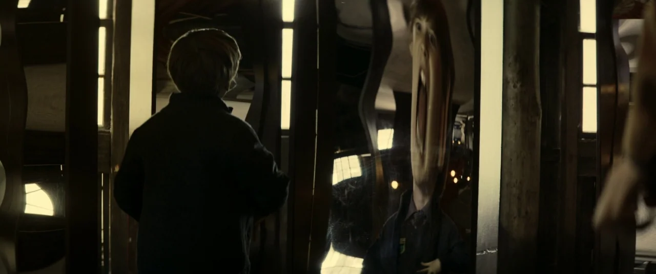 The Hole in the Ground (2019) movie still: medium — A dark interior with tall vertical mirror panels displaying distorted reflections. A boy in a…
