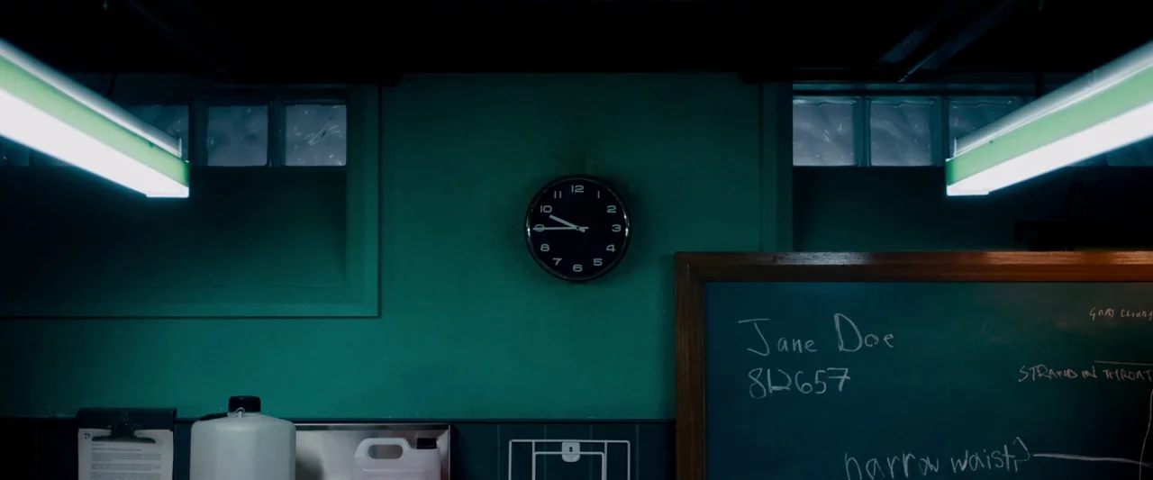 The Autopsy of Jane Doe (2016) movie still: wide — A dark, teal-walled room contains a chalkboard with handwritten case information and an analog…