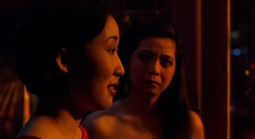Double Happiness (1994) movie still: medium — Two women are positioned in a dark environment with warm, low-key lighting. One woman speaks while the…