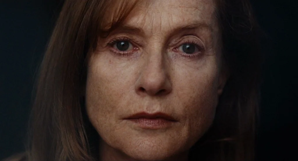 Louder Than Bombs (2015) movie still: closeup — A woman stands in a dimly lit room against a dark, featureless background. She faces forward and…