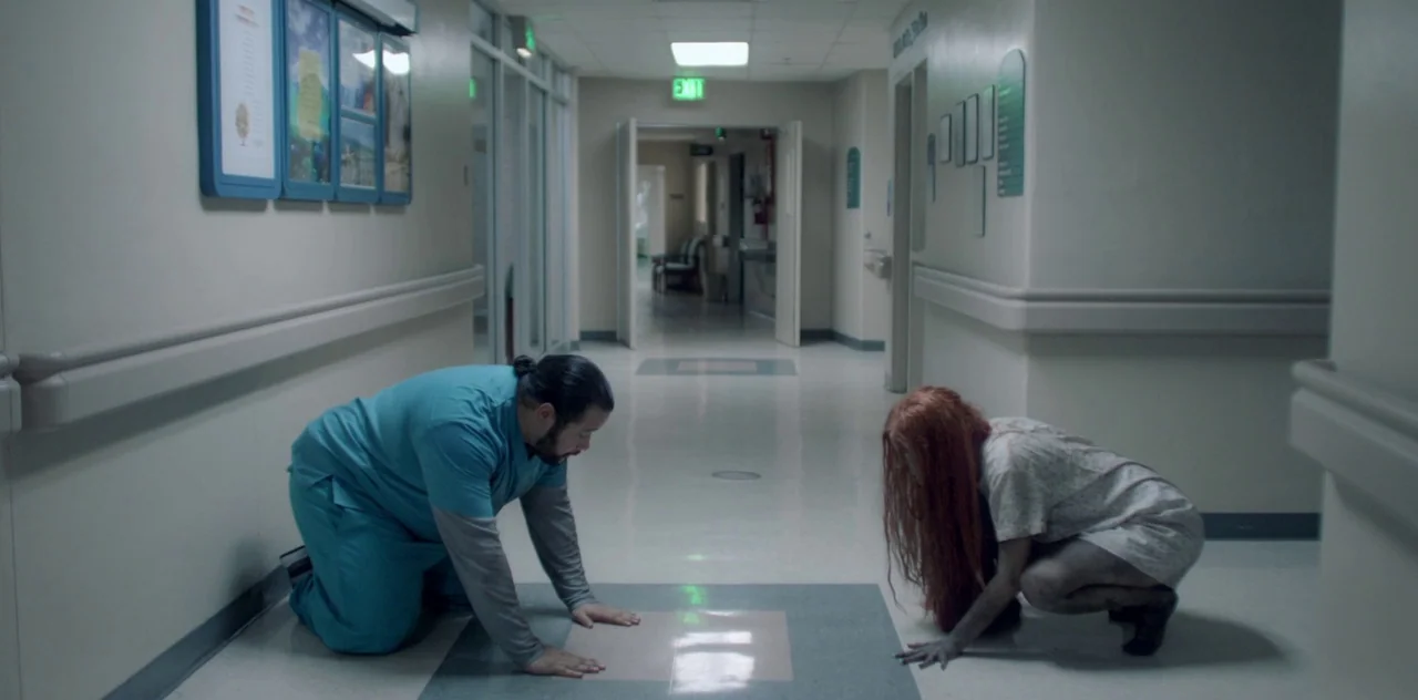 Darlin’ (2019) movie still: wide — A long, brightly lit hospital hallway with linoleum flooring and cream-colored walls. A man in medical scrubs and…