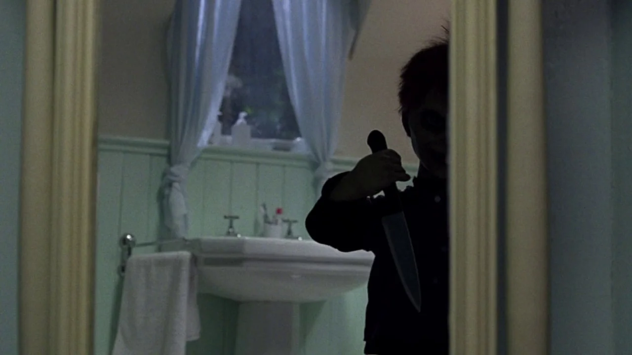Seed of Chucky (2004) movie still: medium — A bathroom featuring a pedestal sink, white curtains, and mint green wainscoting. A dark doll stands in…