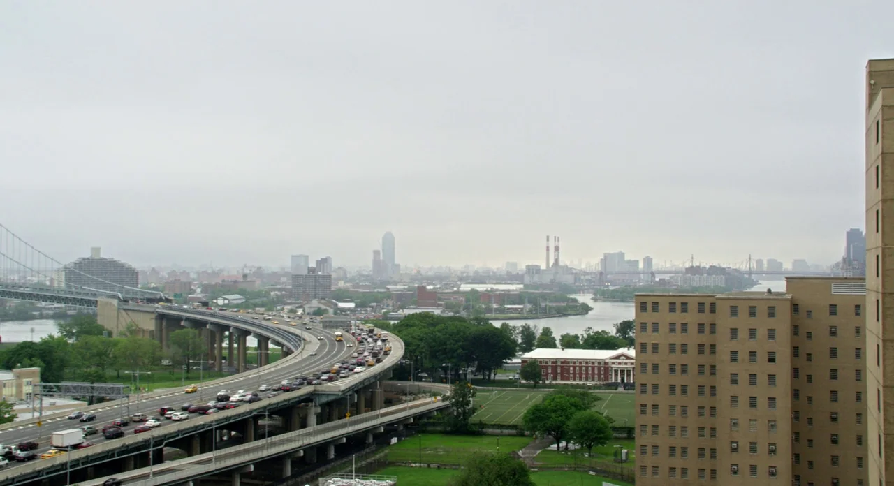 Side Effects (2013) movie still: establishing — An elevated highway curves through a dense urban environment under an overcast grey sky. Numerous…