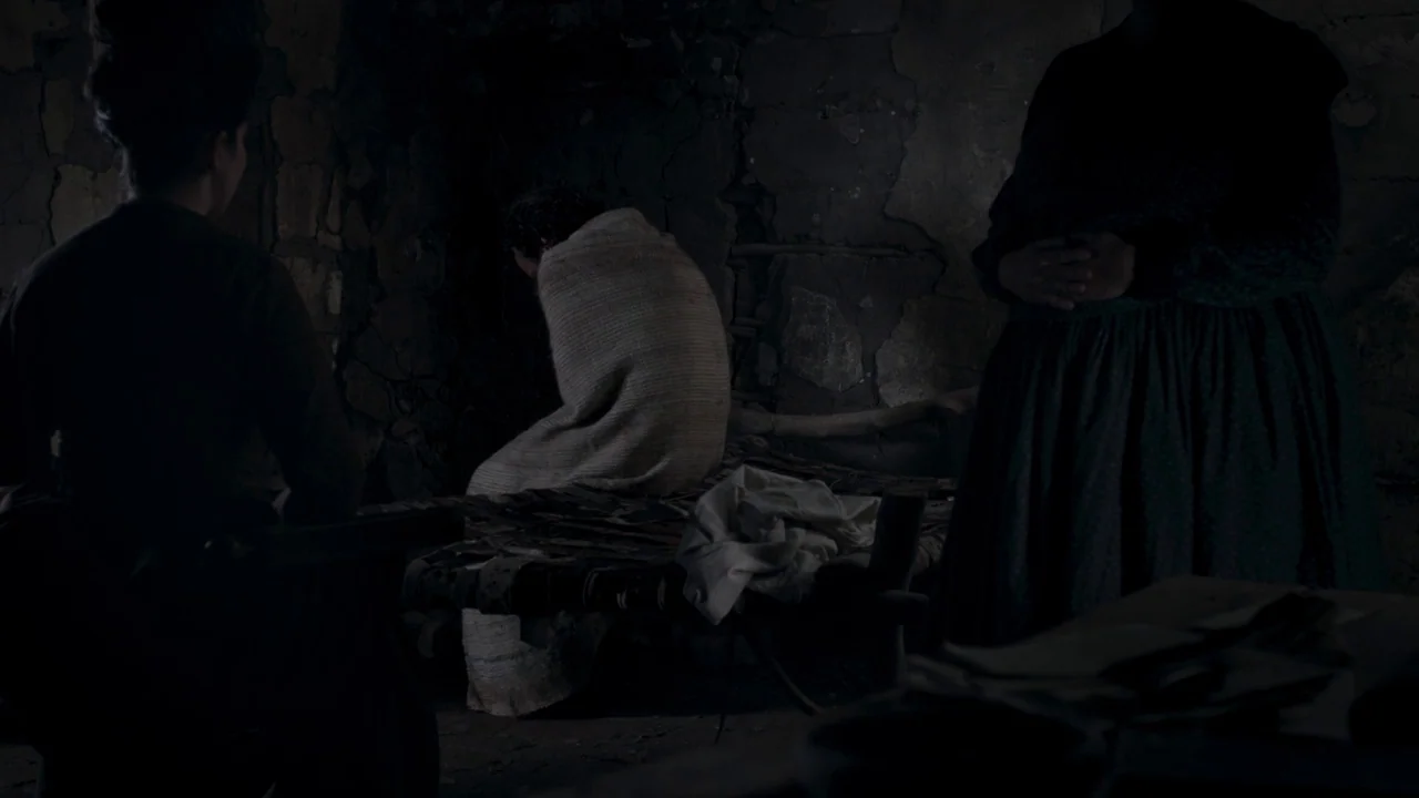 Zama (2017) movie still: medium — A dark, cramped space features crumbling stone walls and a rustic, low-slung bed frame. Three figures stand or sit…