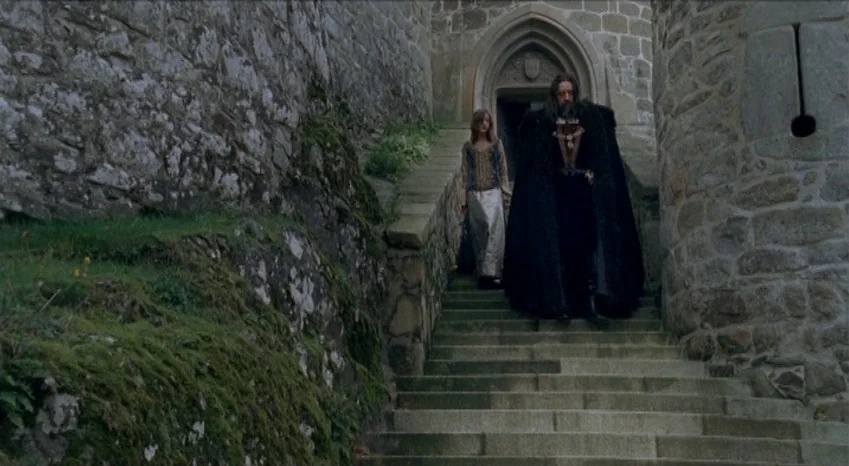 Bluebeard (2009) movie still: fullbody — A stone castle exterior features a high set of stairs flanked by mossy walls. A man in a long dark cloak…