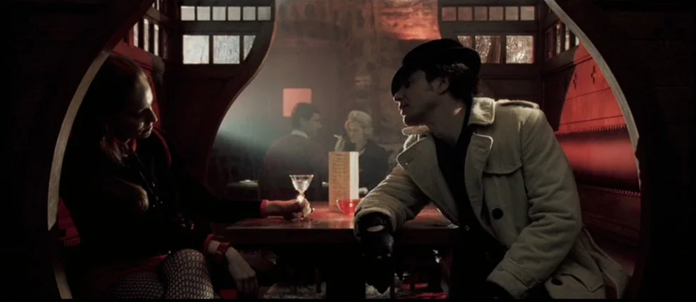 Confessions of a Dangerous Mind (2002) movie still: medium — A dark wooden restaurant booth is bathed in deep red light and thick shadows. A man in…