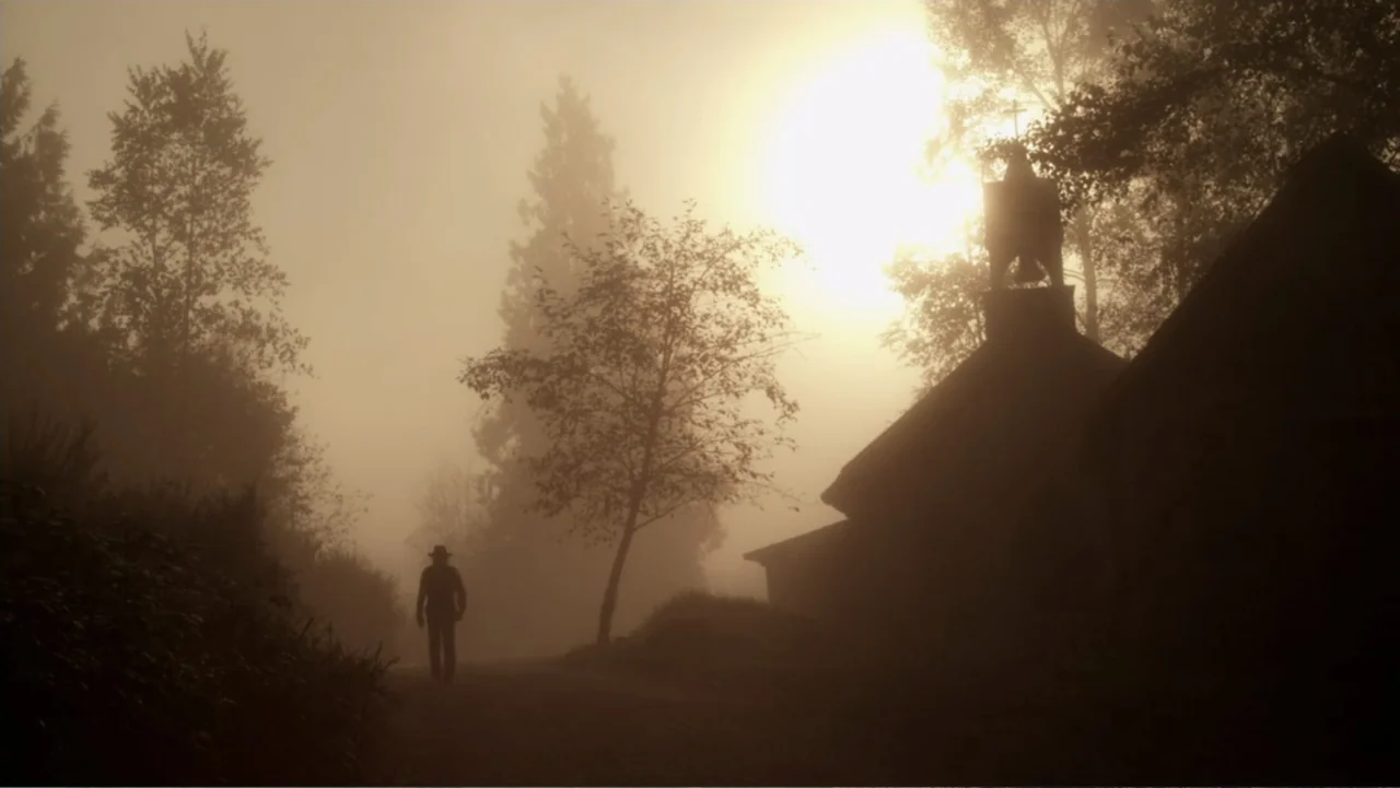 Dawn Rider (2012) movie still: wide — A dense fog covers a path bordered by dark trees and a small structure. A lone figure in a hat walks away into…