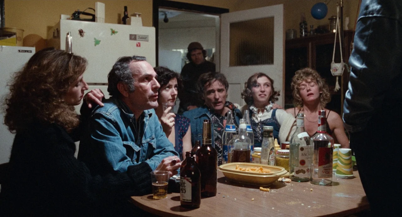 Out of the Blue (1980) movie still: medium — A group of six adults gather around a wooden table in a dimly lit room. Various liquor bottles, snacks…