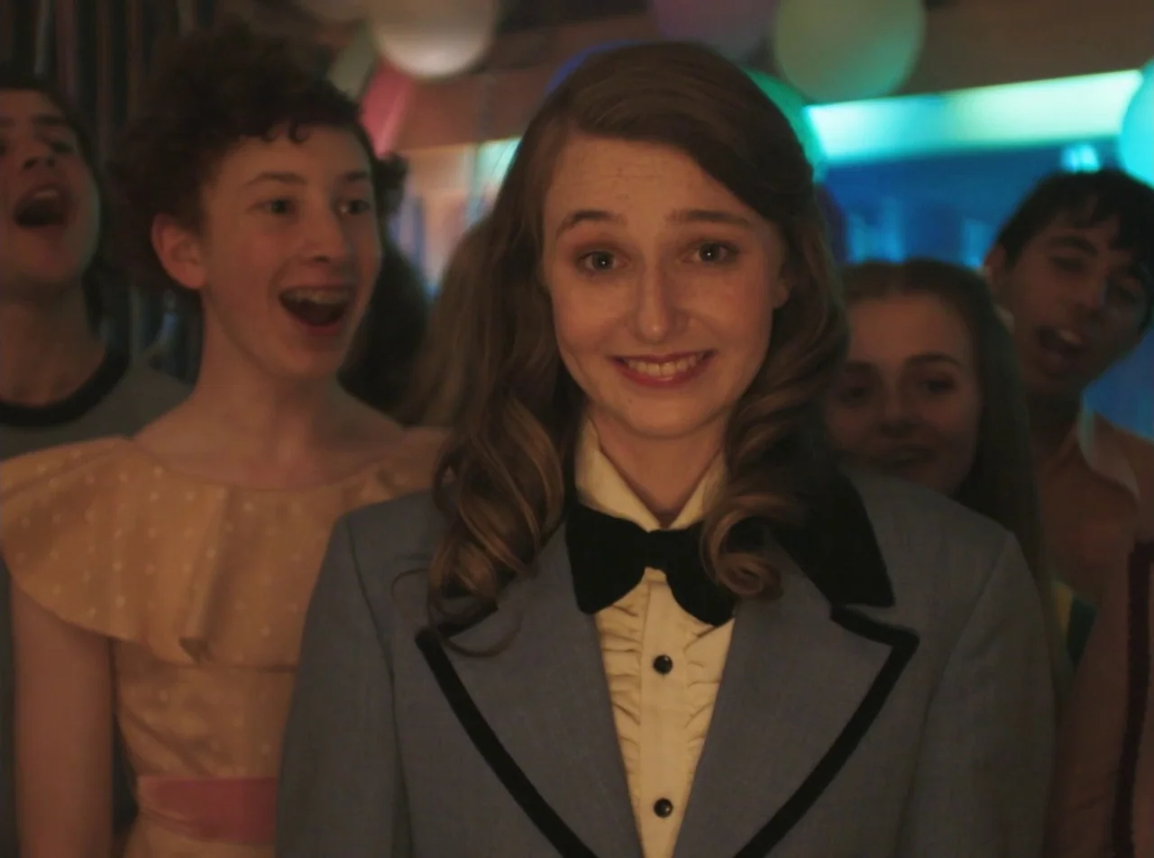 Girl Asleep (2015) movie still: medium — A group of teenagers at a dance with colorful balloons in the background. A young woman with wavy hair…