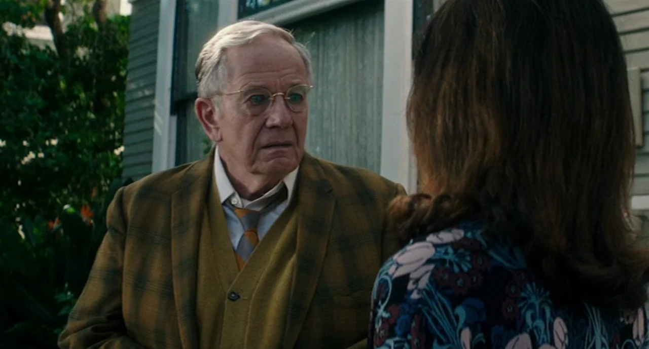 Ouija: Origin of Evil (2016) movie still: medium — An elderly man talks to a woman outside a residential house. The man wears a mustard blazer and…