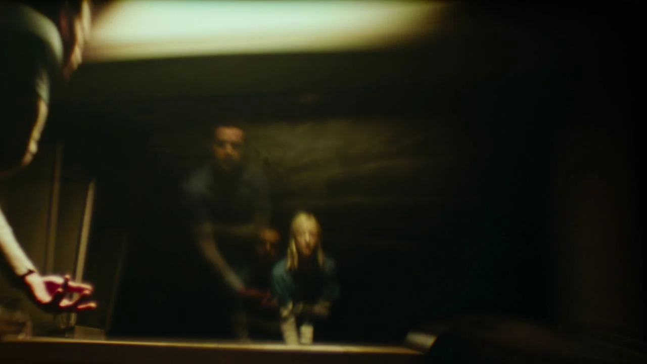Possessor (2020) movie still: medium — A dimly lit room with a reflective surface showing a person looking into it. The subject stands before the…