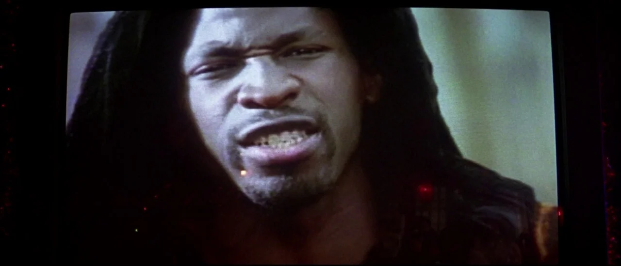 Strange Days (1995) movie still: closeup — A close-up shot of a man's face appearing on a dark television screen. The man has locs and is speaking…