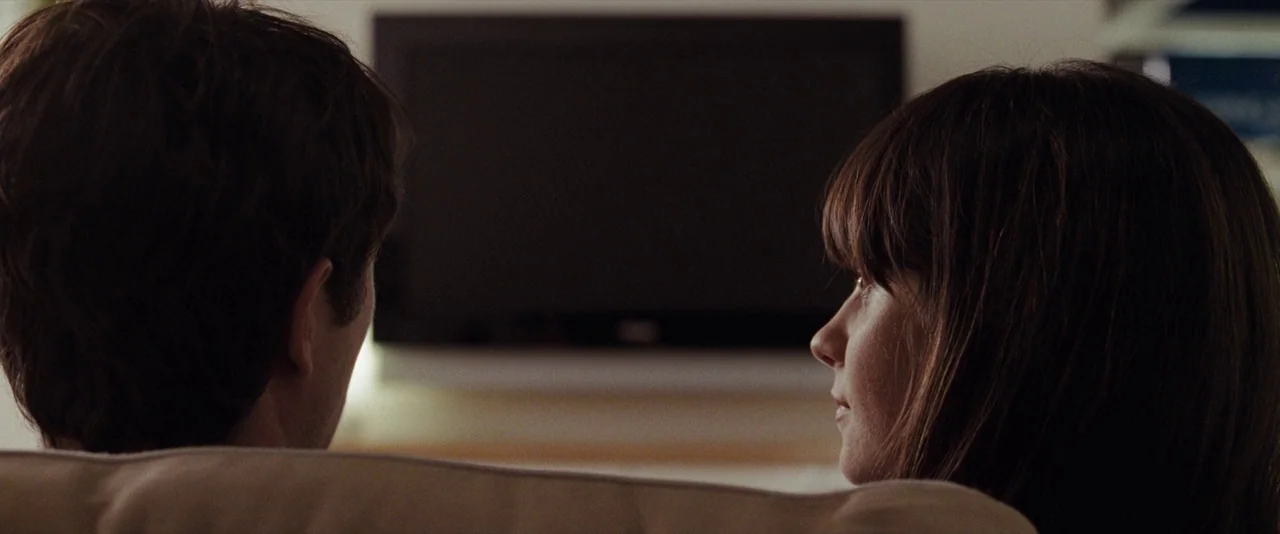 500 Days of Summer (2009) movie still: medium — Two people sit on a couch in a dark room facing a television. They watch the blank screen while…