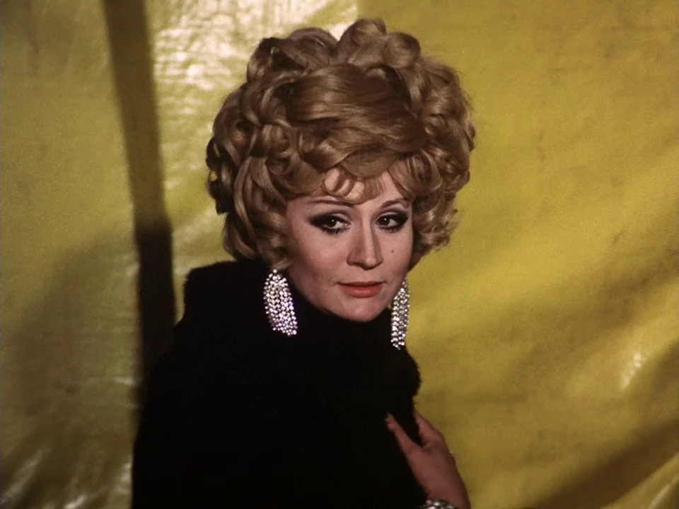 The Clowns (1970) movie still: closeup — A woman stands before a bright yellow fabric backdrop with textured, uneven surfaces. The subject is turned…