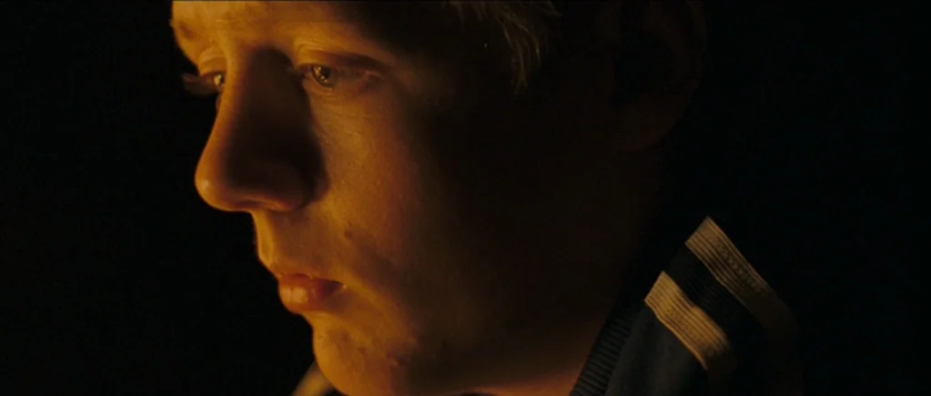 The Scouting Book for Boys (2009) movie still: closeup — A person is situated in a completely dark space. The subject is lit by a warm light while…