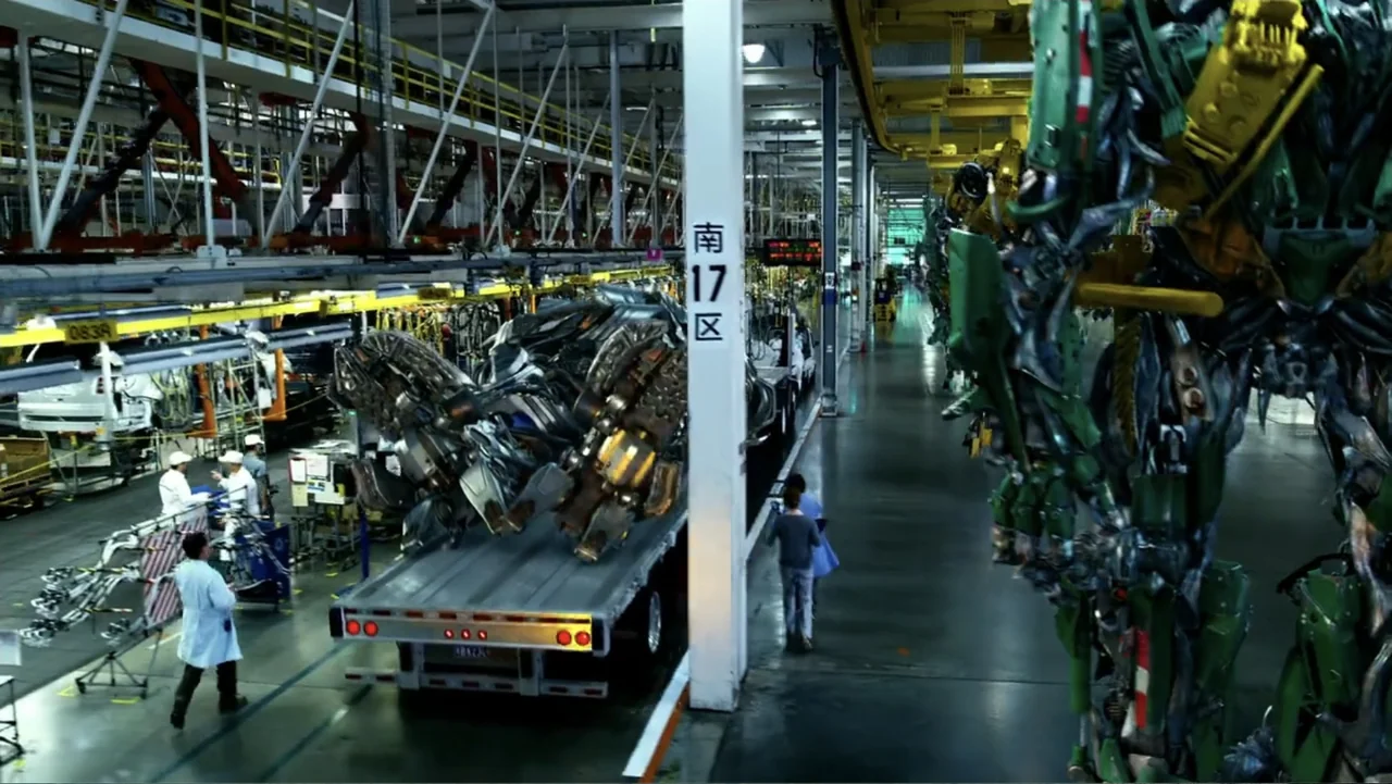 Transformers: Age of Extinction (2014) movie still: wide — A high-ceilinged automotive assembly plant features overhead cranes and white support…