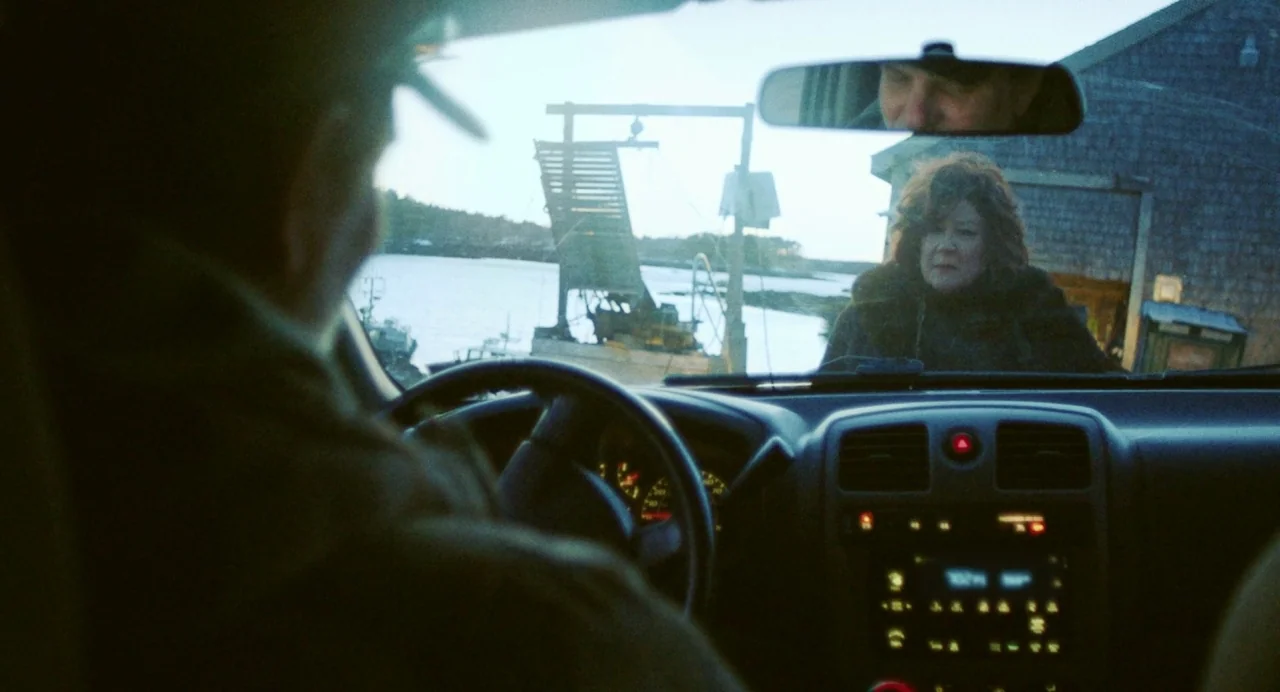 Blow The Man Down (2019) movie still: medium — A man sits in the driver seat of a car looking toward a woman. The woman stands outside the vehicle…