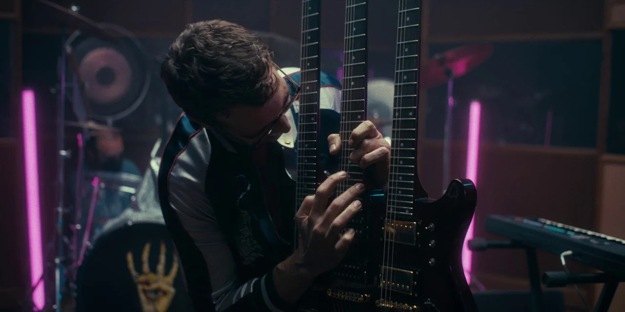 Destroy All Neighbours (2024) movie still: medium — A dark recording studio room features musical equipment including a drum kit and keyboard. A…