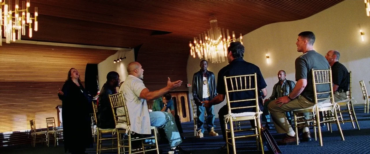 Bad Boys II (2003) movie still: wide — A spacious room with horizontal wooden wall panels features large crystal chandeliers overhead. A diverse…