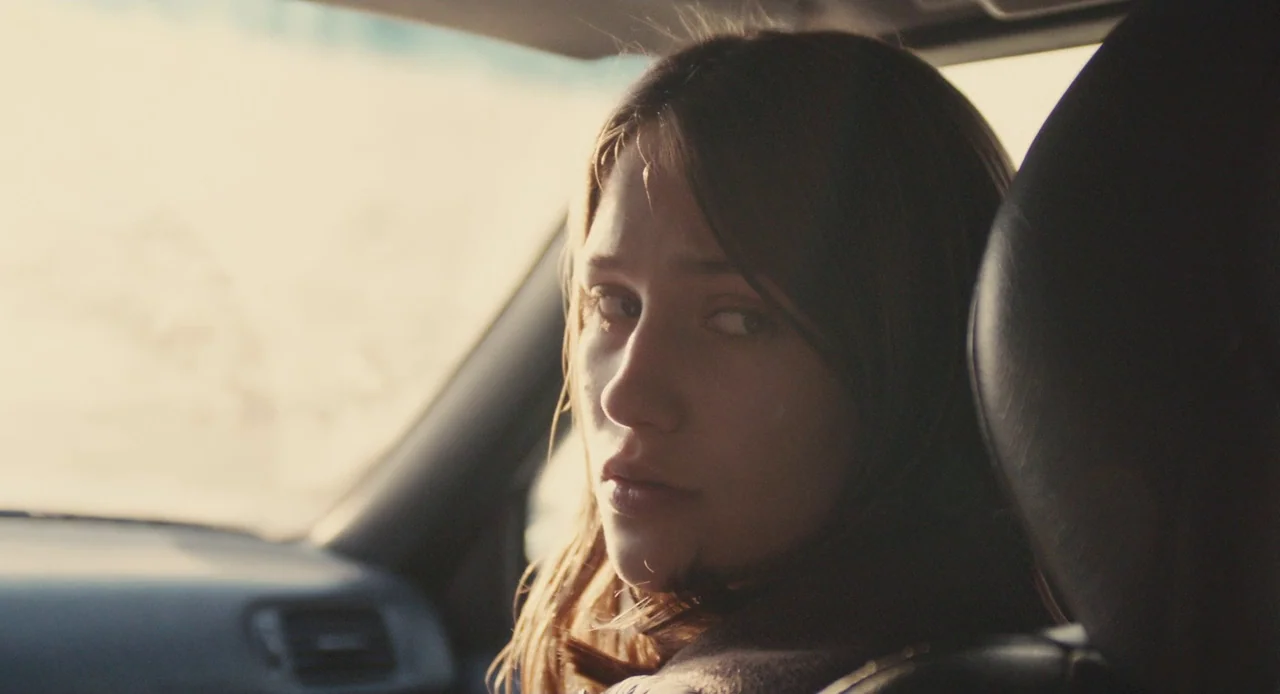 Mistress America (2015) movie still: closeup — A close-up of a woman sitting in the passenger seat of a car. She turns her head to look directly…