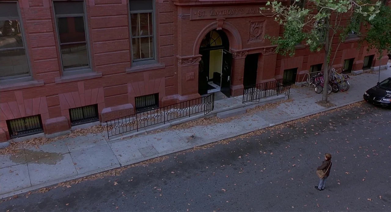 The Sixth Sense (1999) movie still: wide — A red brick building named St. Anthony's Academy stands on a quiet urban street. A lone woman stands on…