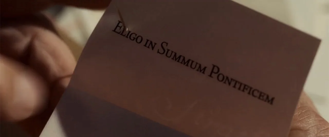Angels & Demons (2009) movie still: closeup — A close up view shows a white paper slip held between fingers. The paper features black printed text…