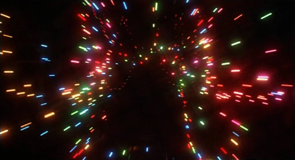 Evil Dead II (1987) movie still: establishing — A vast black void contains a radial burst of multicolored light streaks. The light particles radiate…