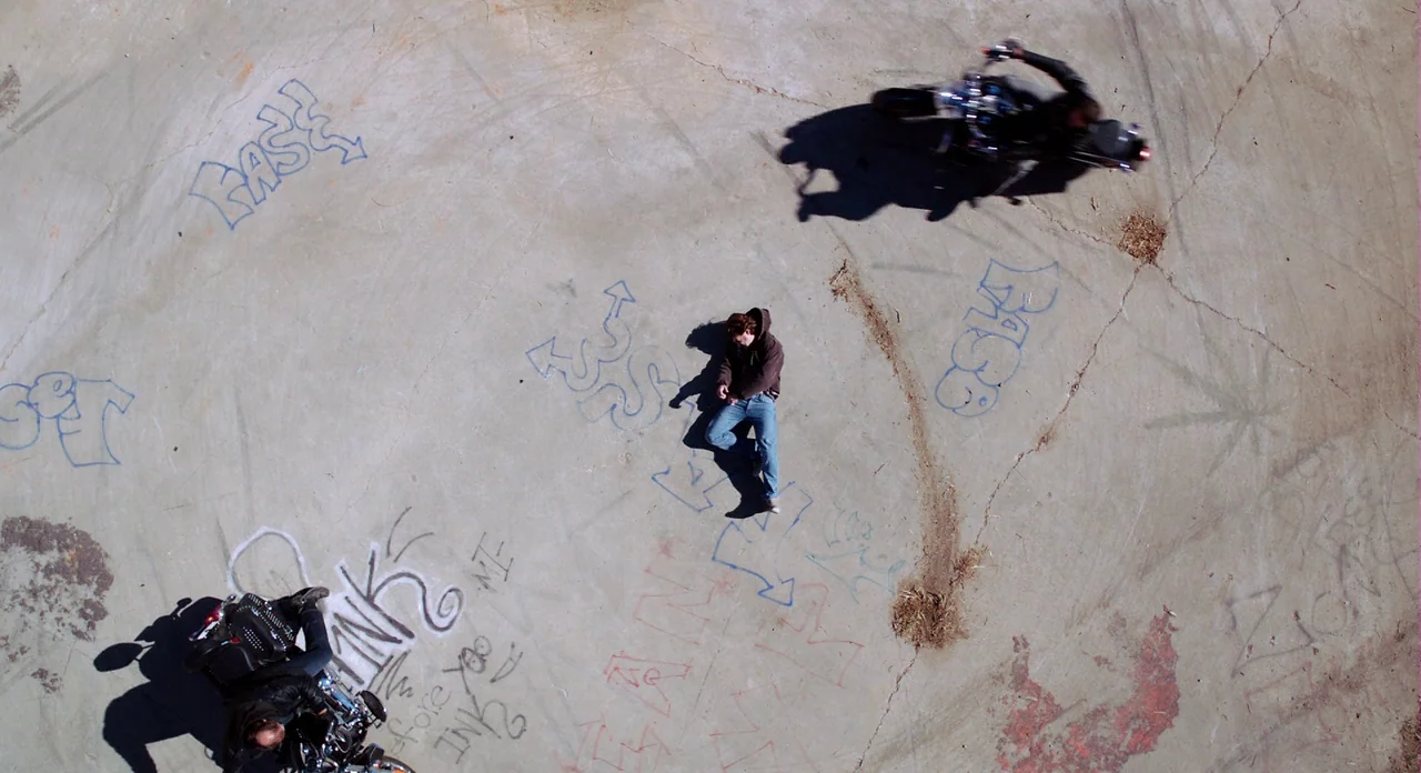 Killer Joe (2011) movie still: wide — A vast, flat expanse of weathered concrete is covered in blue and red spray-painted graffiti. A lone man lies…