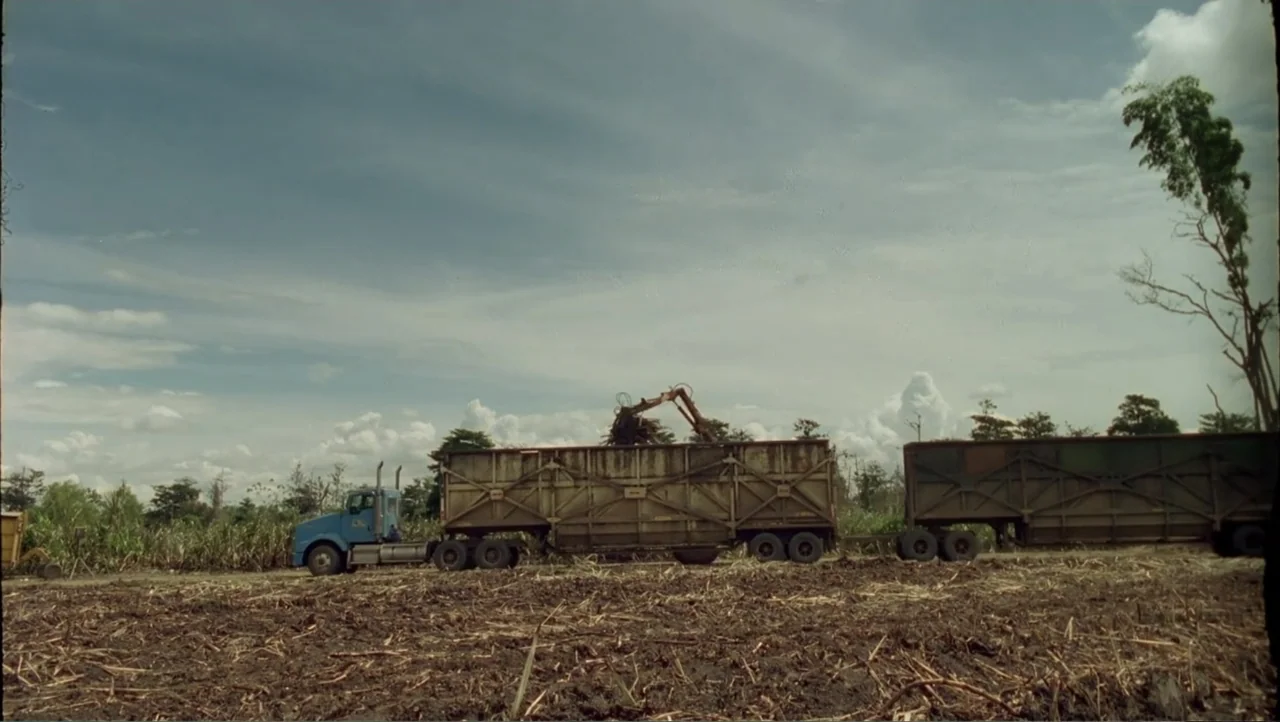 Cut (2000) movie still: wide — A rural agricultural field under a bright sky with scattered clouds. An industrial blue truck with two large metal…