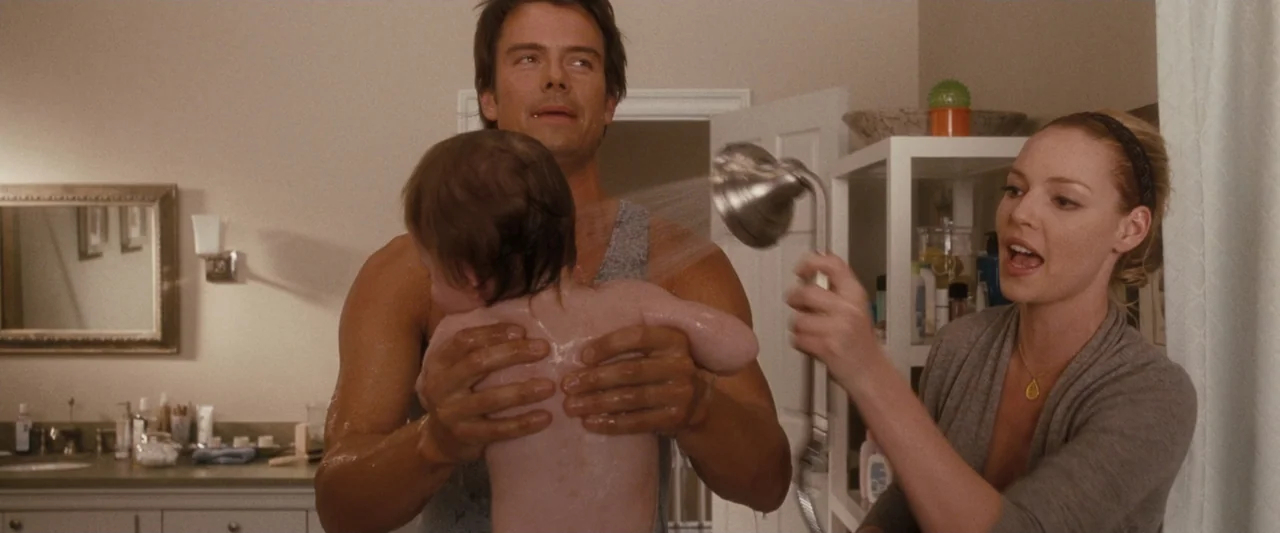 Life As We Know It (2010) movie still: medium — A residential bathroom with beige walls and a white vanity mirror visible in background. A man holds…