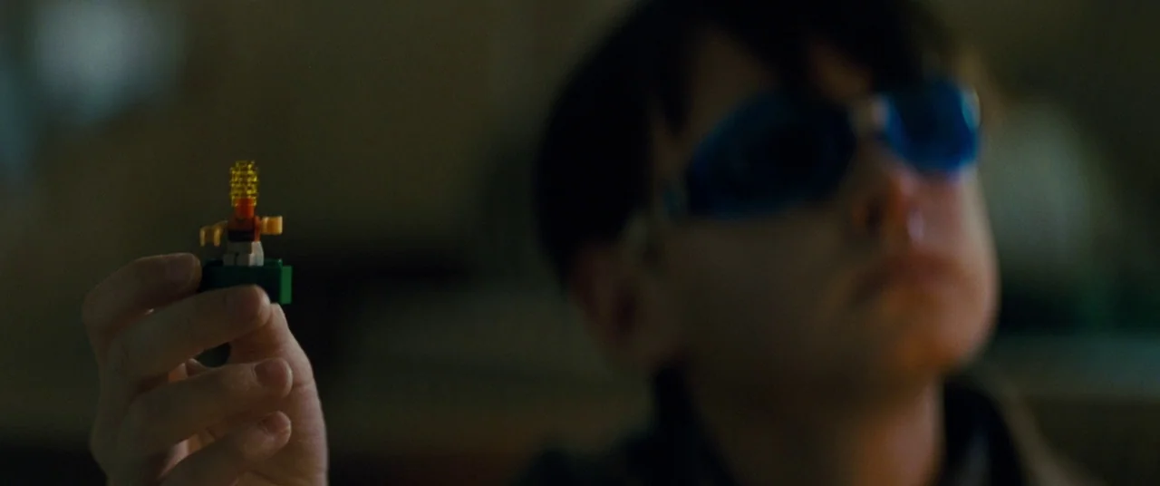 Midnight Special (2016) movie still: closeup — A dimly lit room with a child in the background out of focus. The child wears blue swim goggles while…