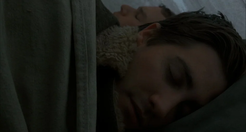Brokeback Mountain (2005) movie still: closeup — Two men sleep close together beneath a thick, textured canvas tent fabric. They lie shoulder to…