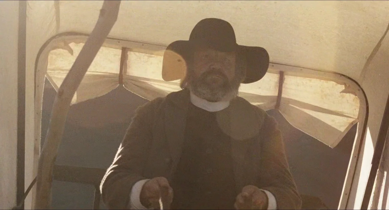 Breaker Morant (1980) movie still: medium — An older man sits under the canvas canopy of a moving wooden wagon. He holds the leather reins and…