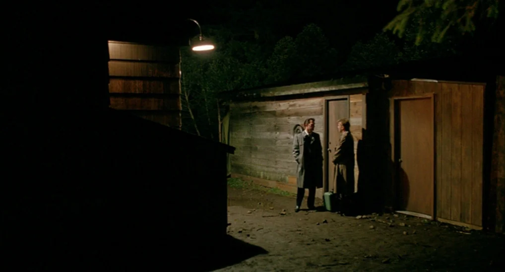 Twin Peaks: Fire Walk With Me (1992) movie still: wide — Two men stand near a wooden shed in a dark, wooded outdoor space at night. They stand in…