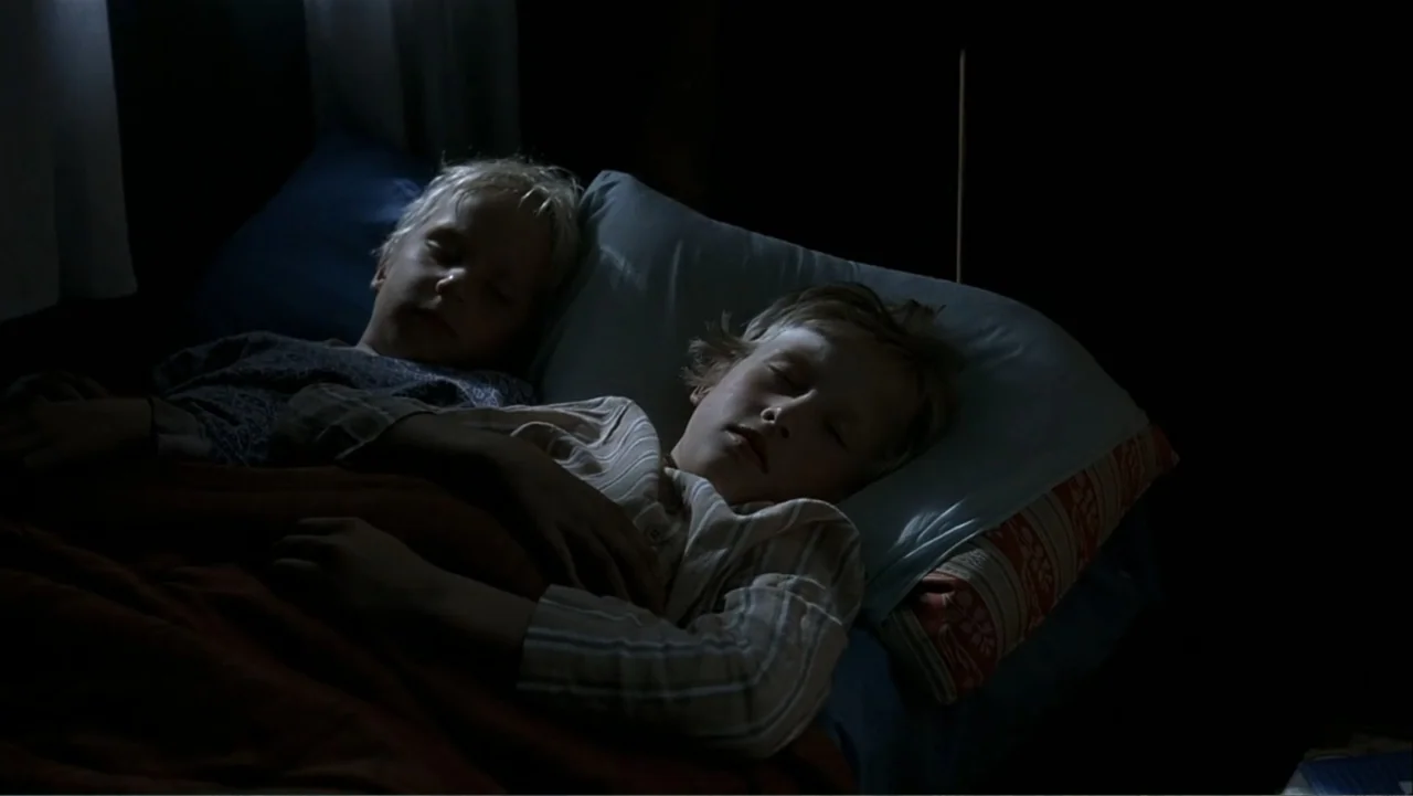 The Man Without a Past (2002) movie still: medium — Two young boys rest together on pillows within a dimly lit space. They sleep soundly under a…